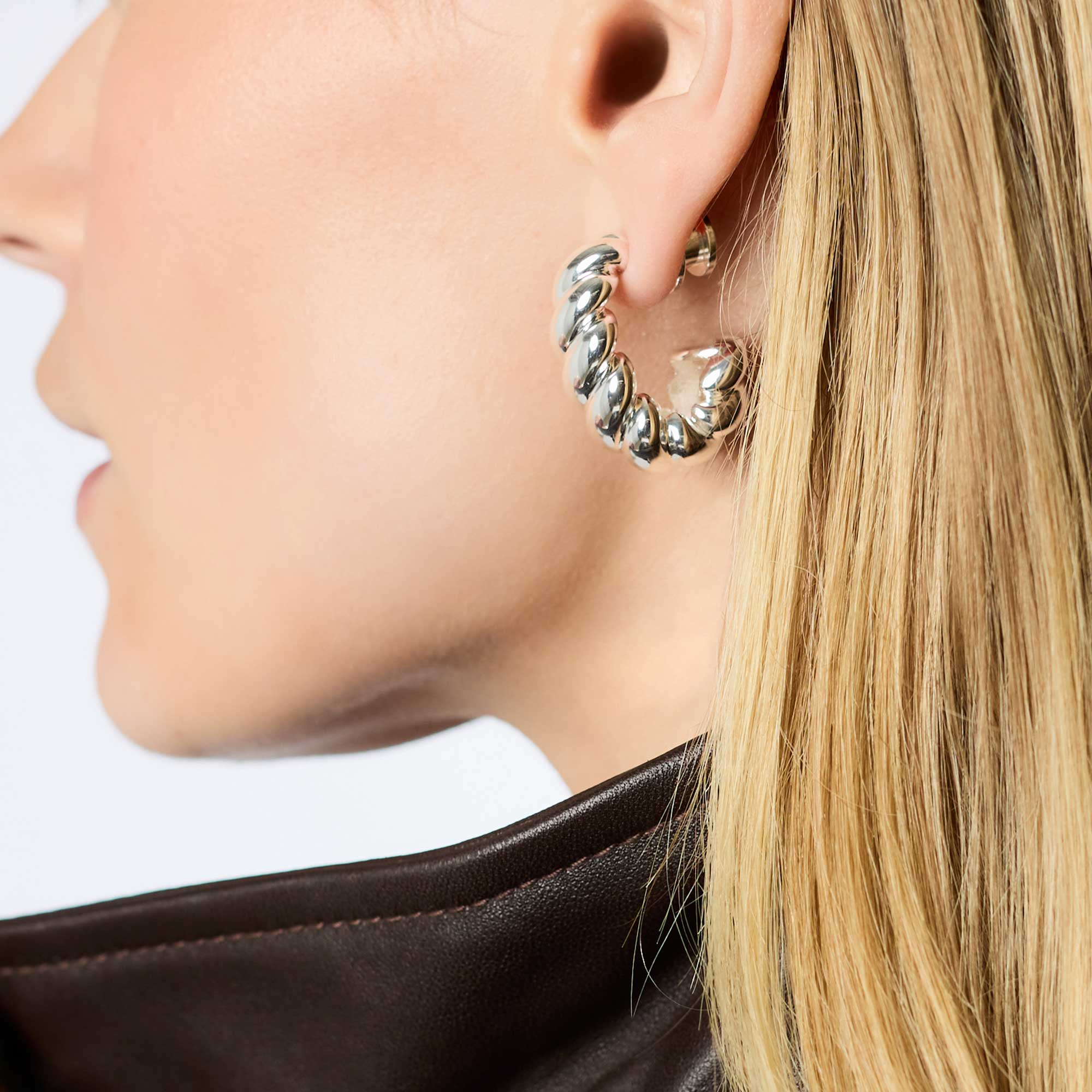 A person wearing a Ravello Statement Hoop, a thick silver-plated twisted hoop earring.