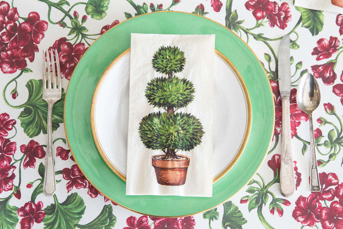 White guest napkin featuring a green three-tiered topiary tree in a terracotta pot.