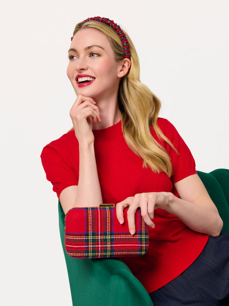 A woman in a red top holding a red tartan plaid Scottie Minaudière clutch with gold hardware.