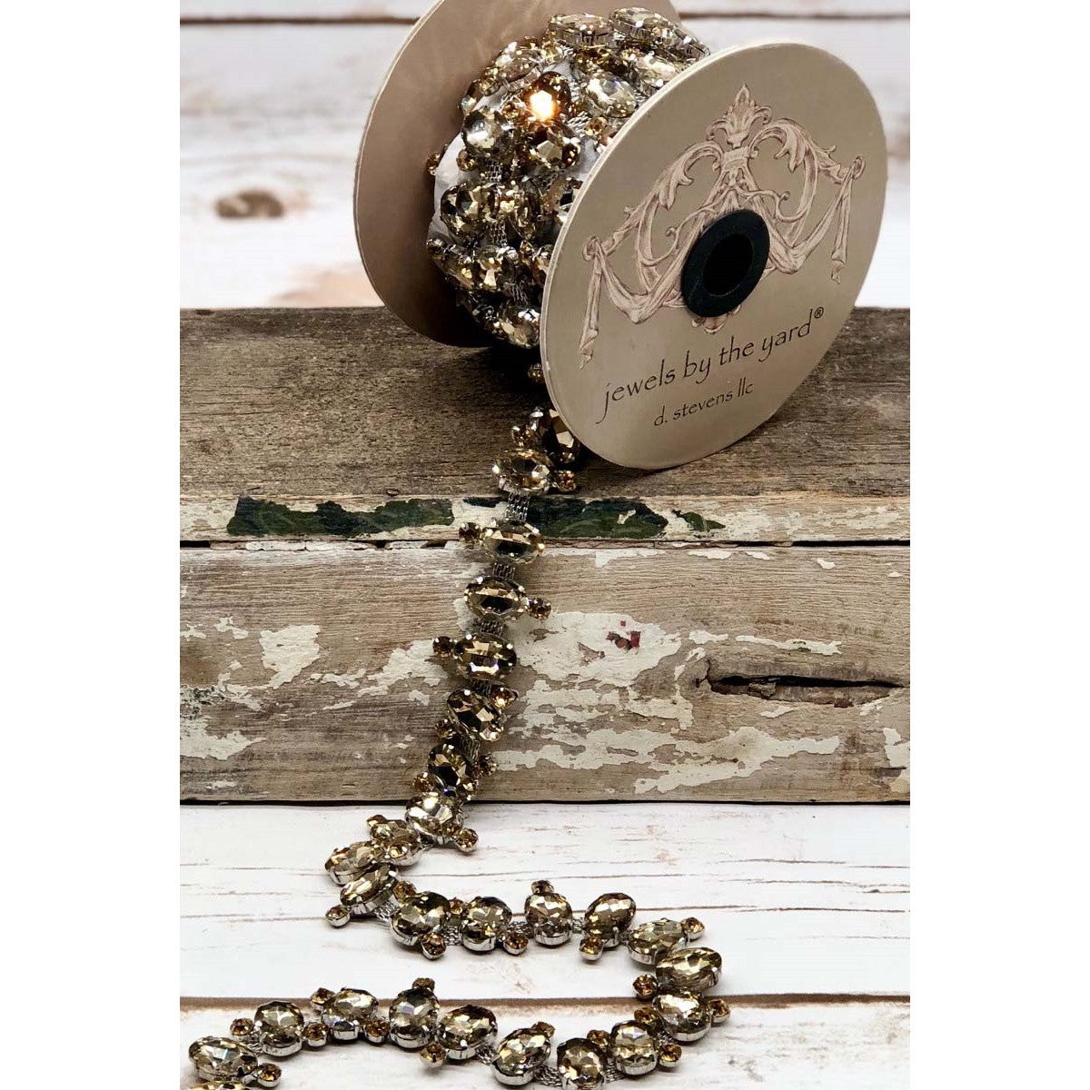 Large oval smoke-colored rhinestone trim on a spool and draped over rustic wood.