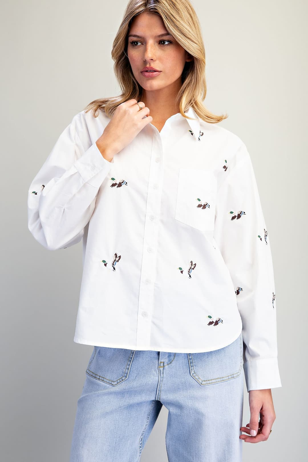 Woman wearing a white long-sleeve button-down shirt with an all-over embroidered mallard duck motif.
