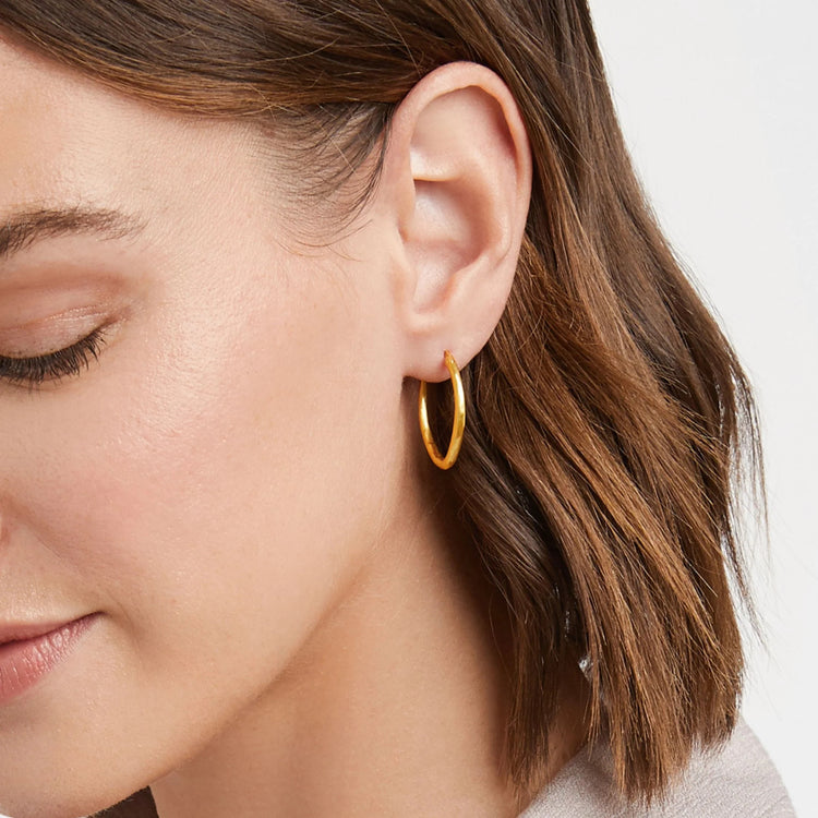 Close-up of a person wearing a gold hoop earring from the Fleur-de-Lis 2-in-1 Earring set.