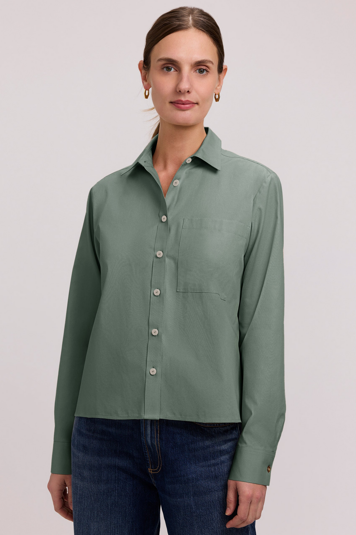 Woman wearing a sage green Jodie No Iron Pinpoint long sleeve short shirt with dark blue jeans.