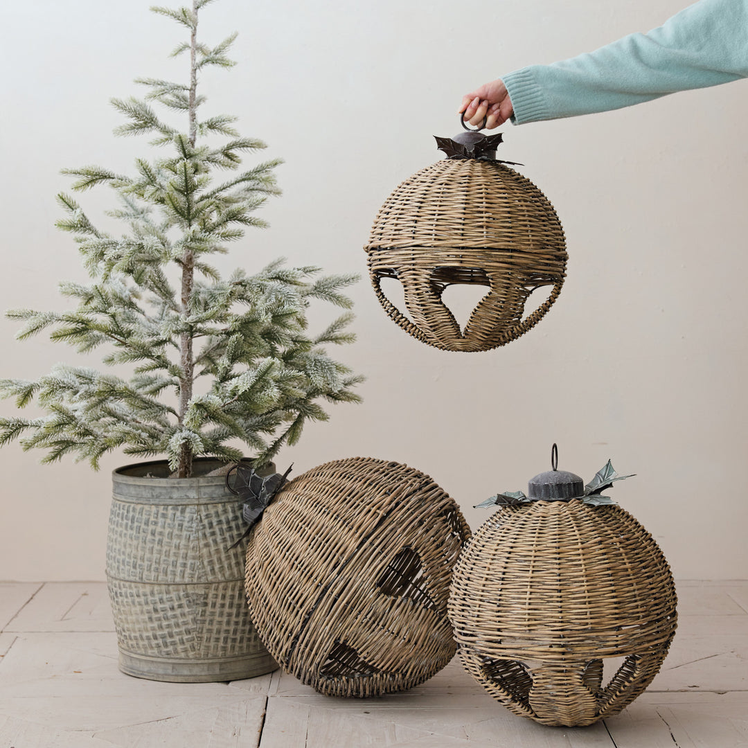 Three oversized hand-woven rattan bells with metal leaf details next to a small frosted pine tree.