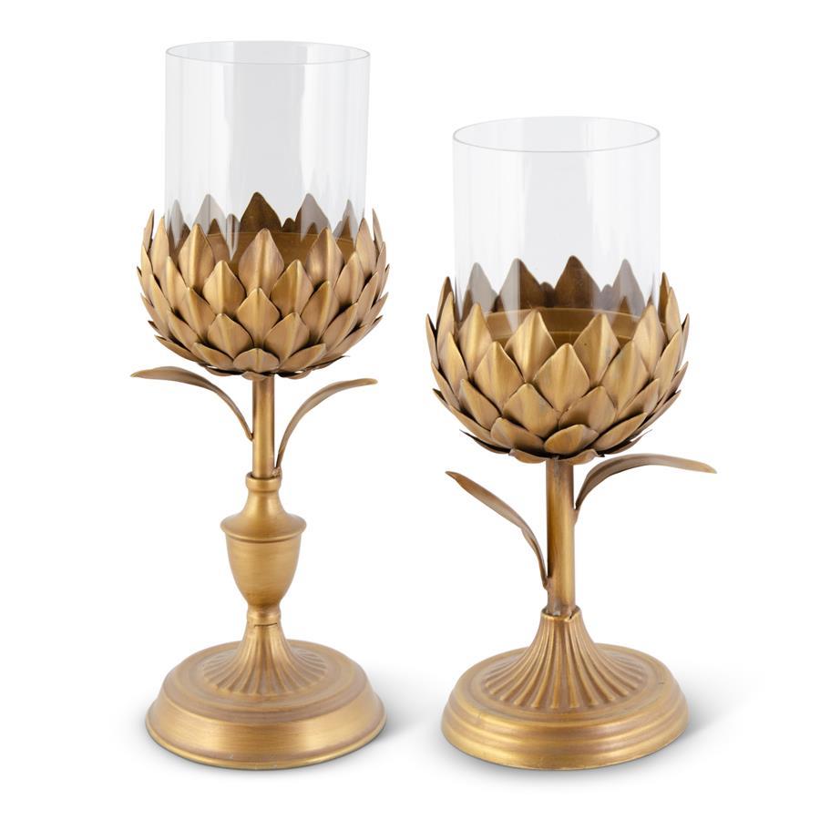 Two gold petal candleholders with glass cylinders on round bases in varying heights.