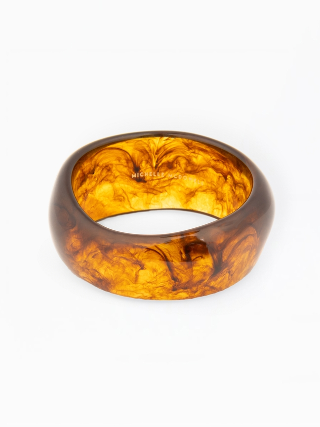 Sally Bangle, a wide tortoise shell resin bracelet with amber and brown marbled patterns.