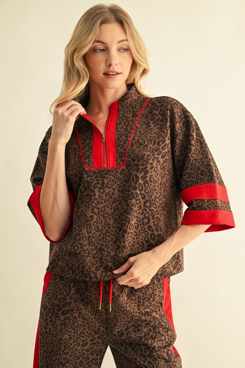 Woman wearing a brown leopard print faux suede top with red contrast trim and a half-zip neckline.