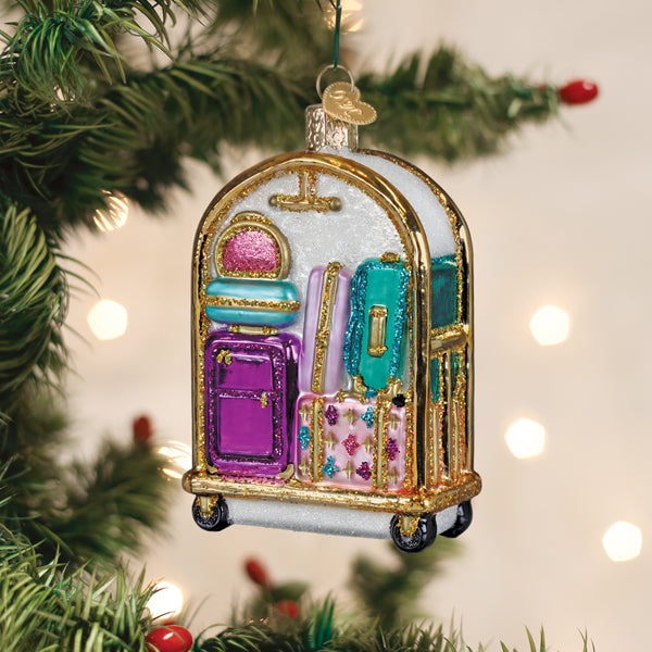 Glass hotel luggage cart ornament with colorful glittery suitcases hanging on a Christmas tree.