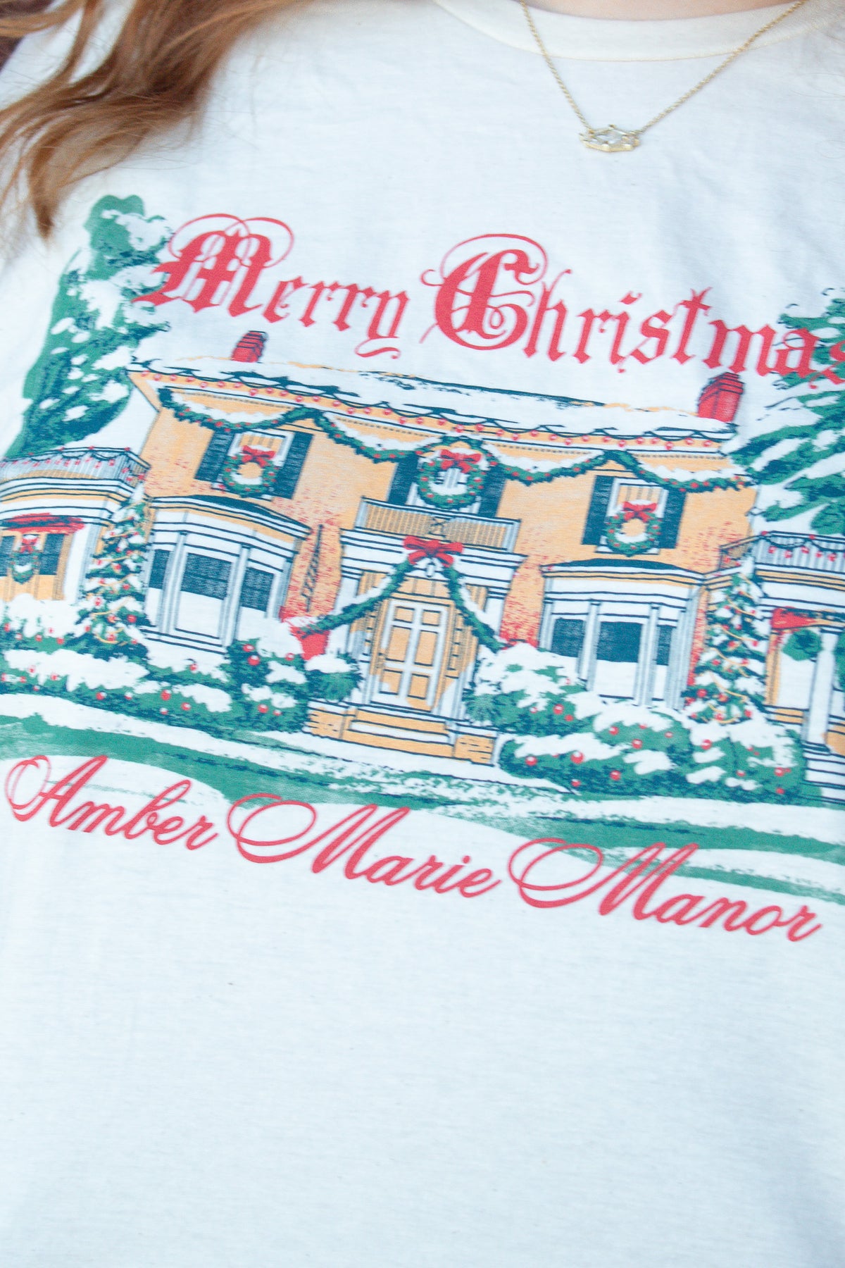 Ivory Christmas t-shirt featuring an illustration of a decorated manor with the text Merry Christmas Amber Marie Manor.
