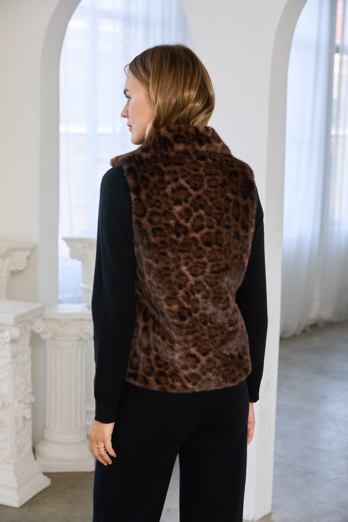 Back view of a woman wearing the Celeste Leopard Faux Fur Vest over a black long-sleeve top.
