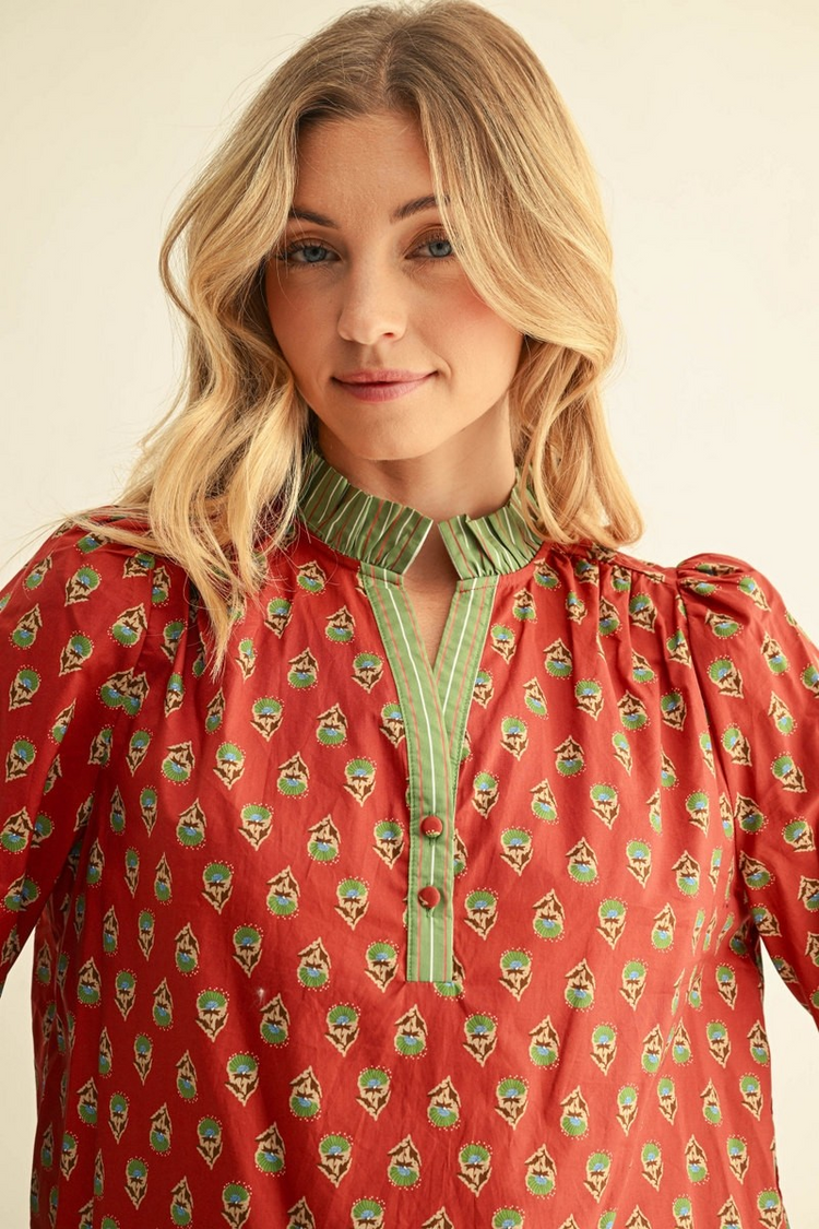 Woman wearing a red floral top with green striped ruffle collar and notched V-neckline.