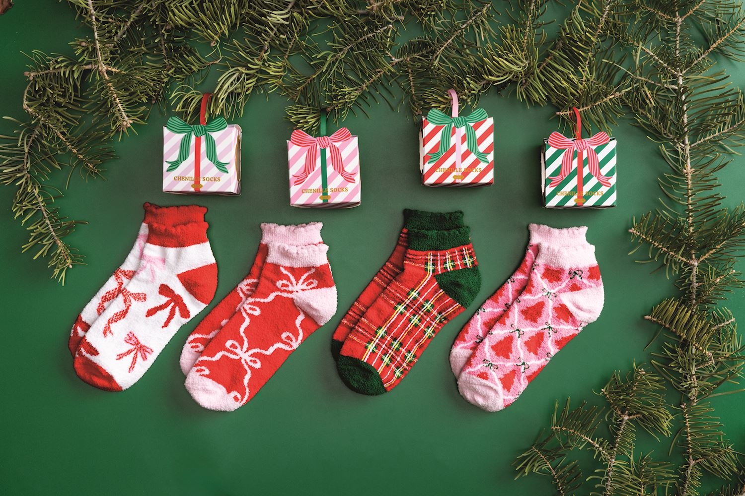 Four pairs of patterned chenille holiday socks displayed with matching ornament gift boxes.