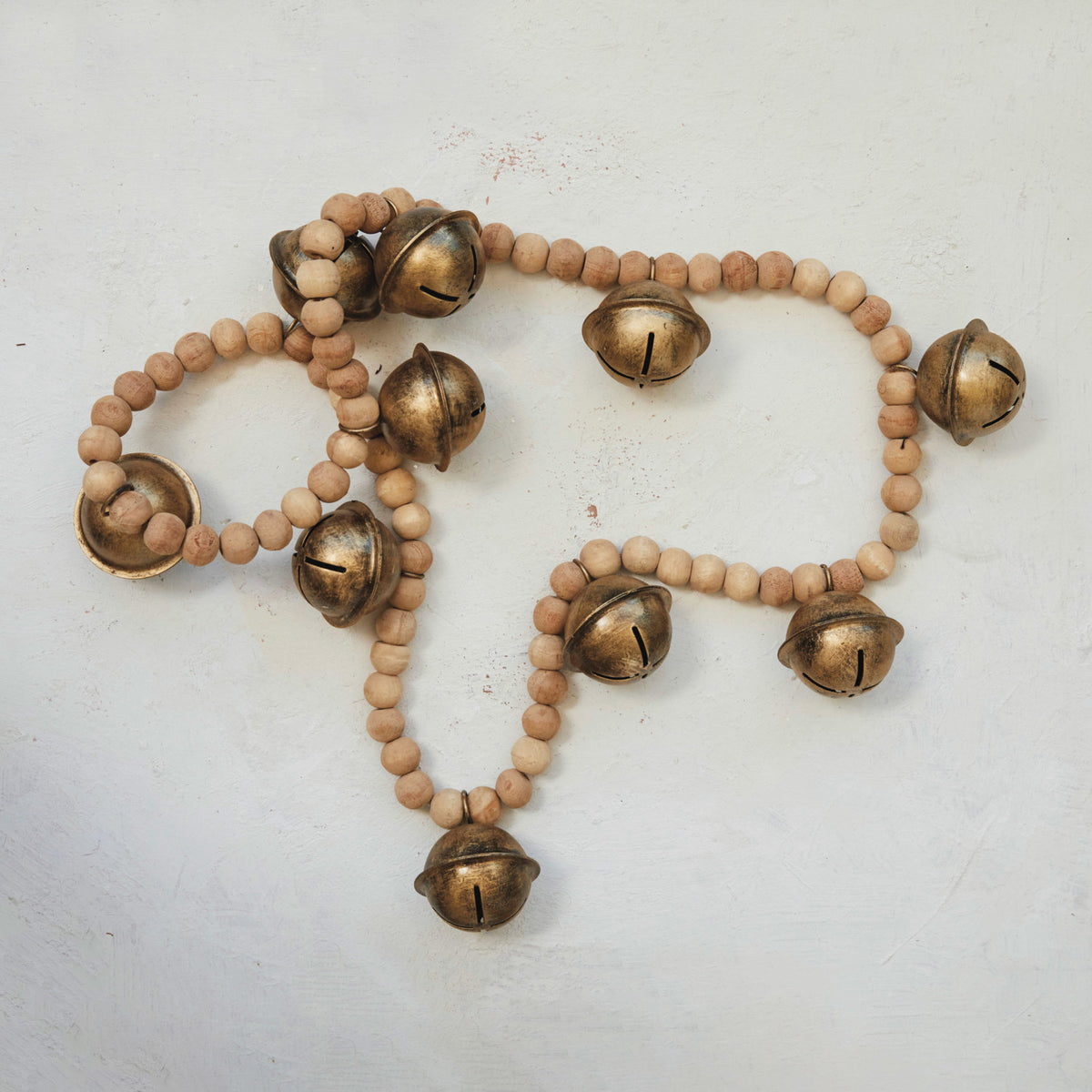 Natural wood bead garland with antique gold finish metal bells on a white surface.