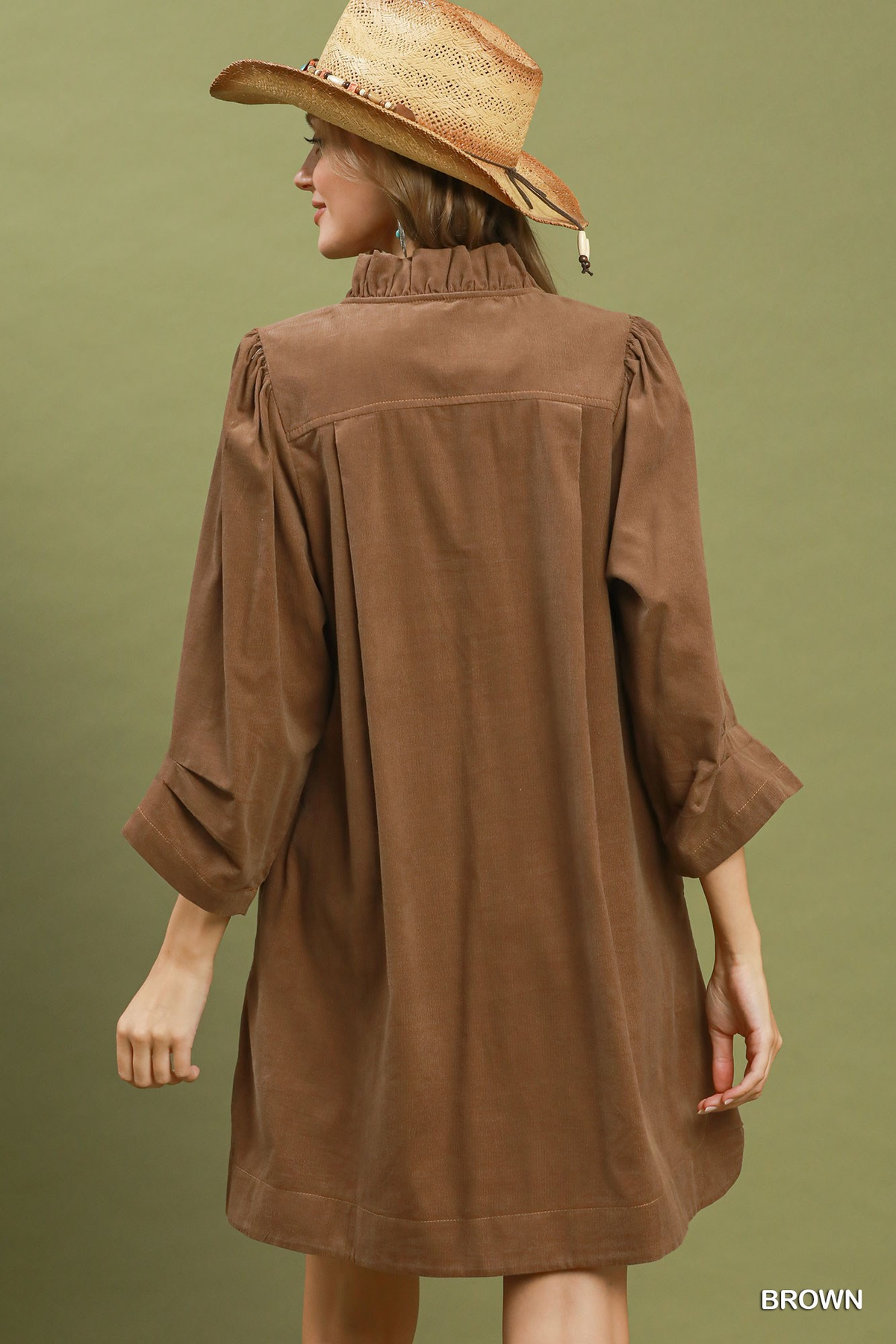 Back view of a woman wearing a brown corduroy split neck puff sleeve shift dress and a straw hat.