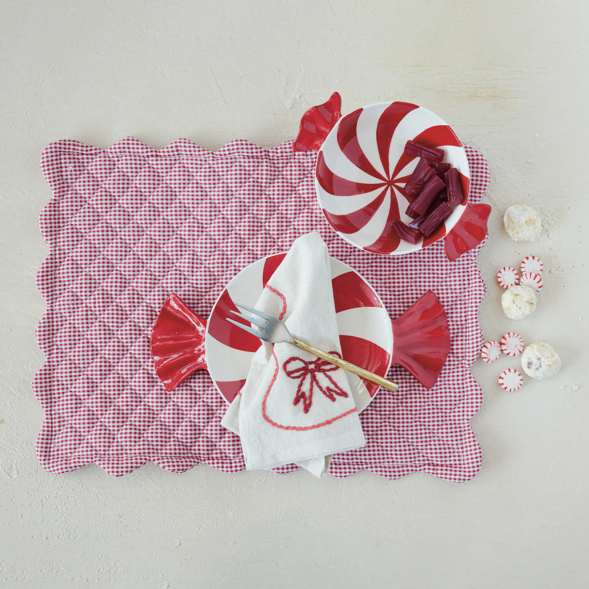 Hand-painted red and white peppermint swirl ceramic candy-shaped bowl on a red checkered placemat.