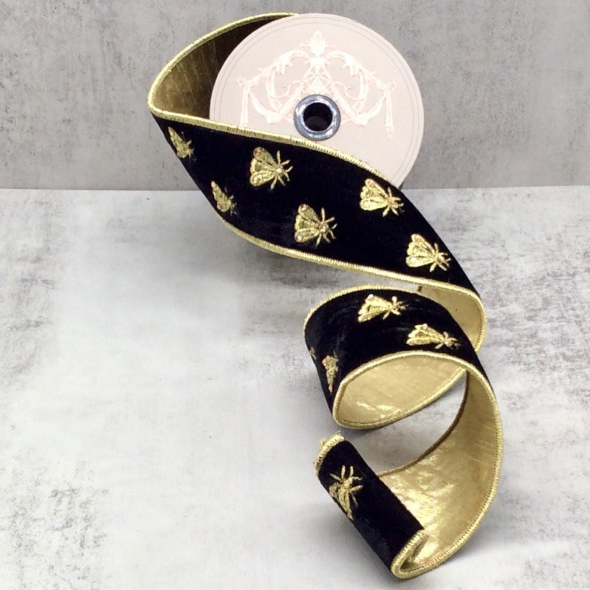 2.5 inch black velvet ribbon with gold embroidered bees and gold metallic backing on a spool.