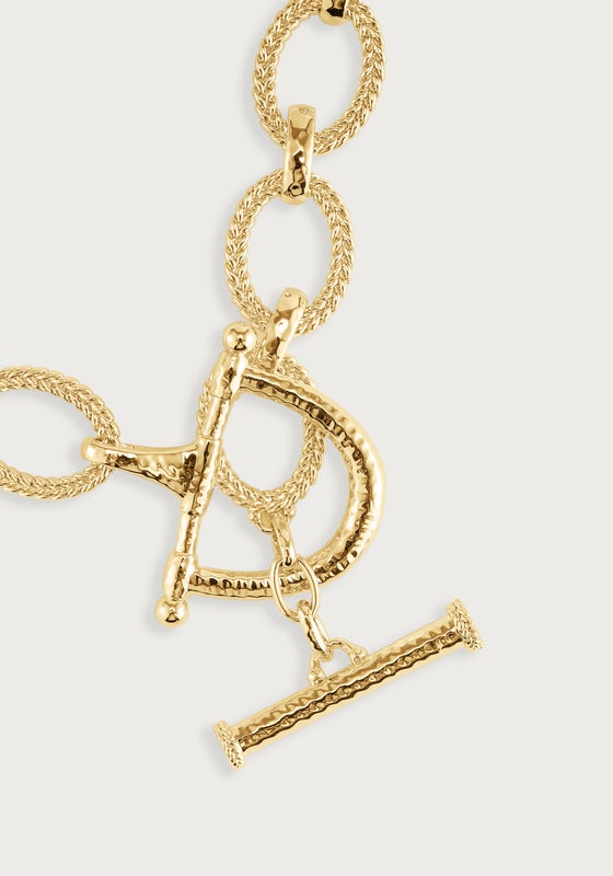 Close-up of a gold-plated braided chain lariat necklace featuring a sculptural toggle clasp.