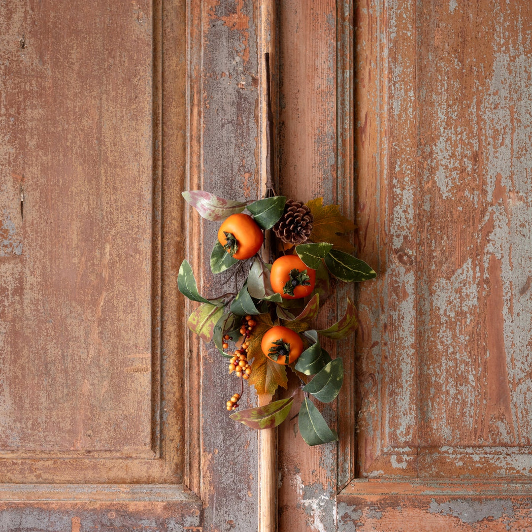Autumn persimmon pick with orange fruit, green leaves, and a pinecone on a rustic wooden background.