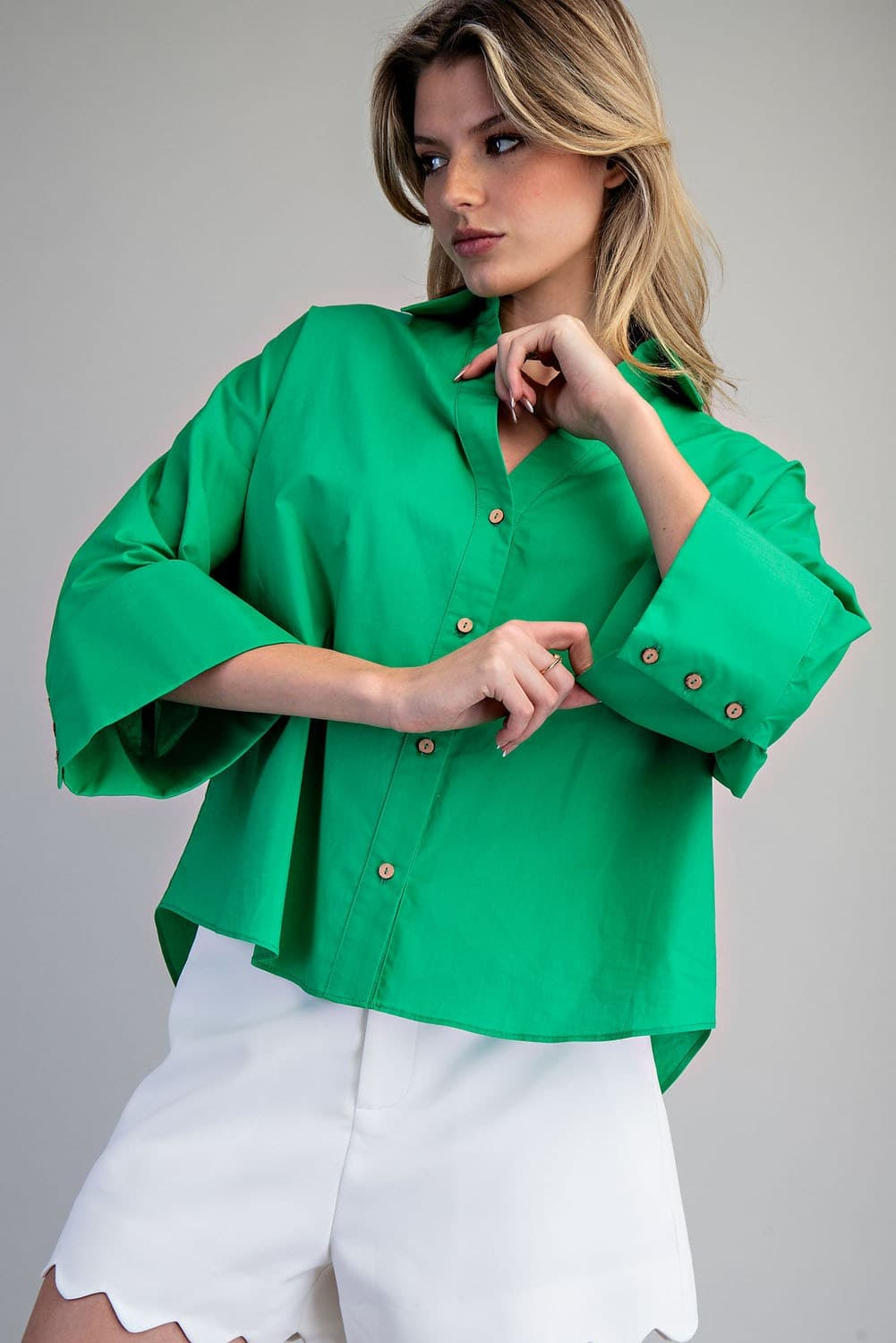 Woman wearing a green Blake Back Pleat Button Down Blouse with wide sleeves and white shorts.