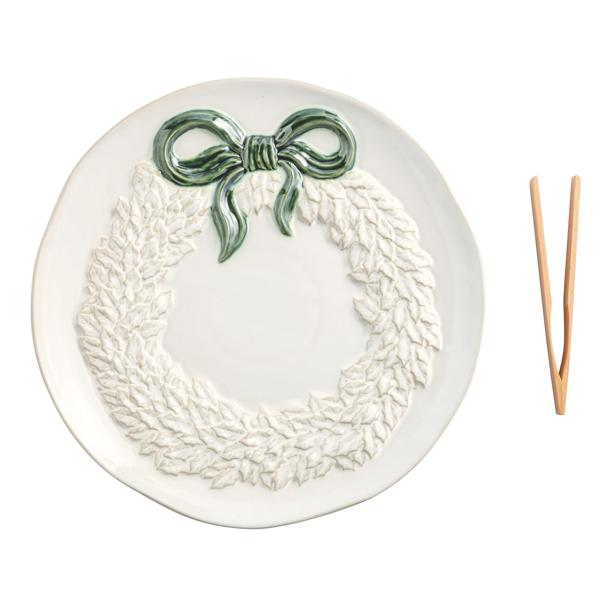 White ceramic wreath cookie plate with a green bow and wooden tongs.