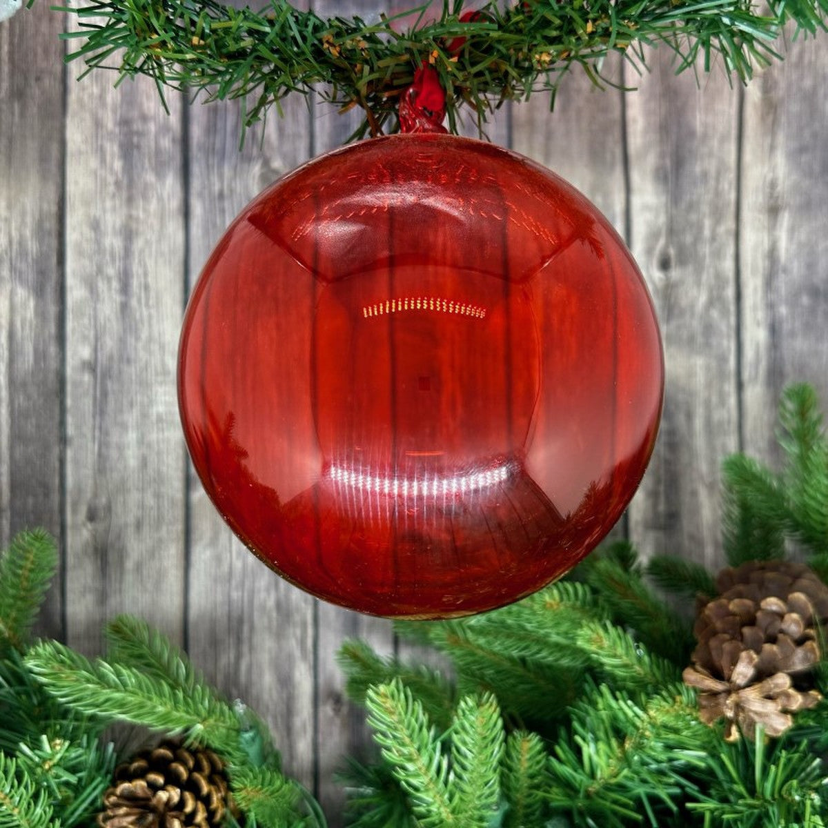150mm red hand-blown glass ornament hanging from a green garland with pinecones.