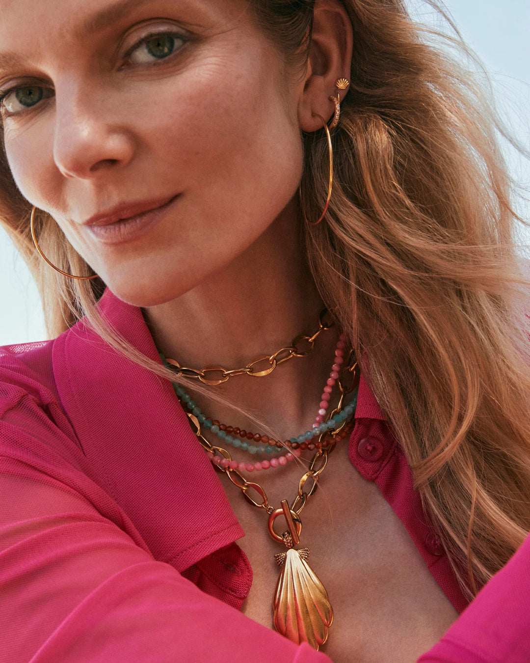 Woman wearing the Sylvia Strand Necklace, a gold chain with a shell pendant and colorful beads.