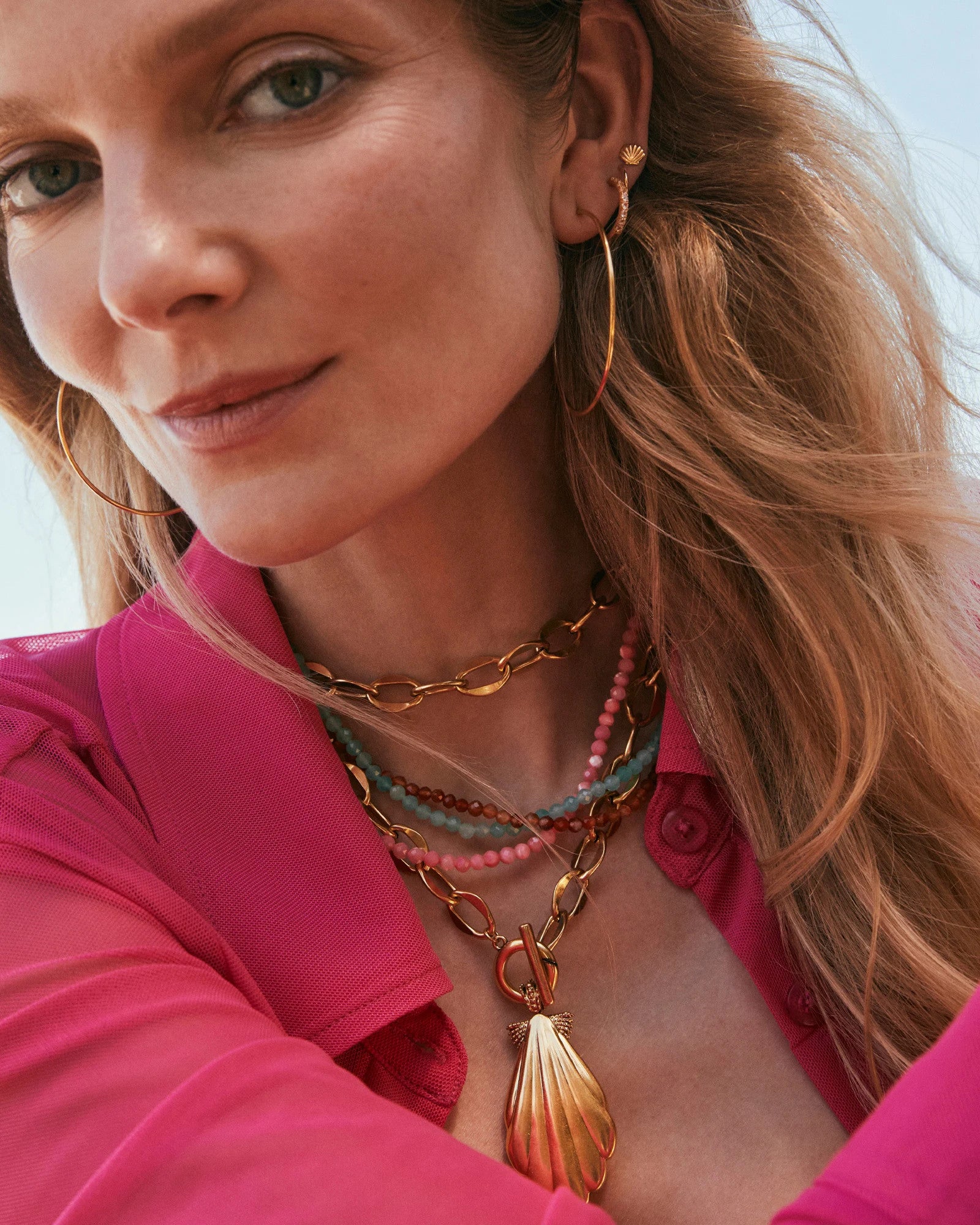 Woman wearing the Sylvia Strand Necklace, a gold chain with a shell pendant and colorful beads.