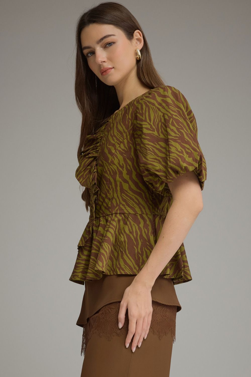 Woman wearing a brown and olive green zebra print top with short puff sleeves and ruffled front.