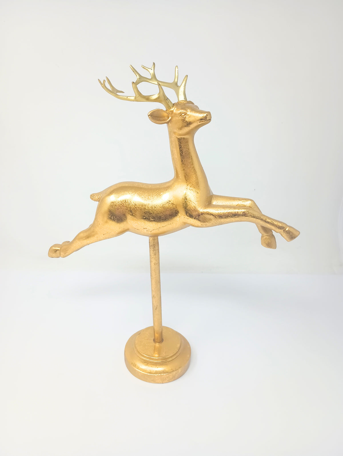 Gold flying reindeer figurine on a matching pedestal stand against a white background.