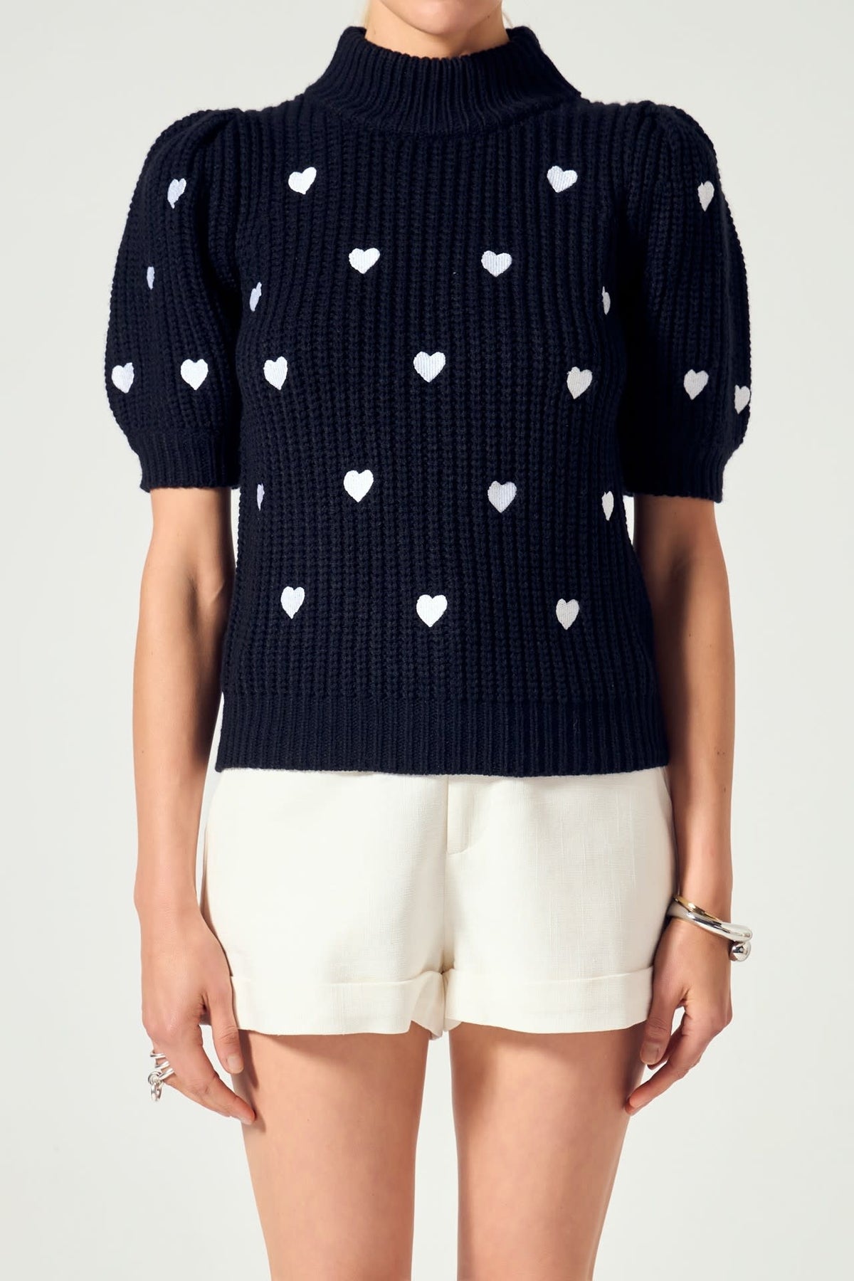 Black acrylic knit sweater with heart embroidery on puffy sleeves and mock neck.