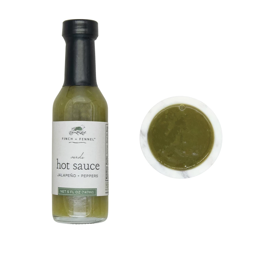 A 5 oz bottle of Finch + Fennel Verde Hot Sauce next to a small bowl of the green sauce.