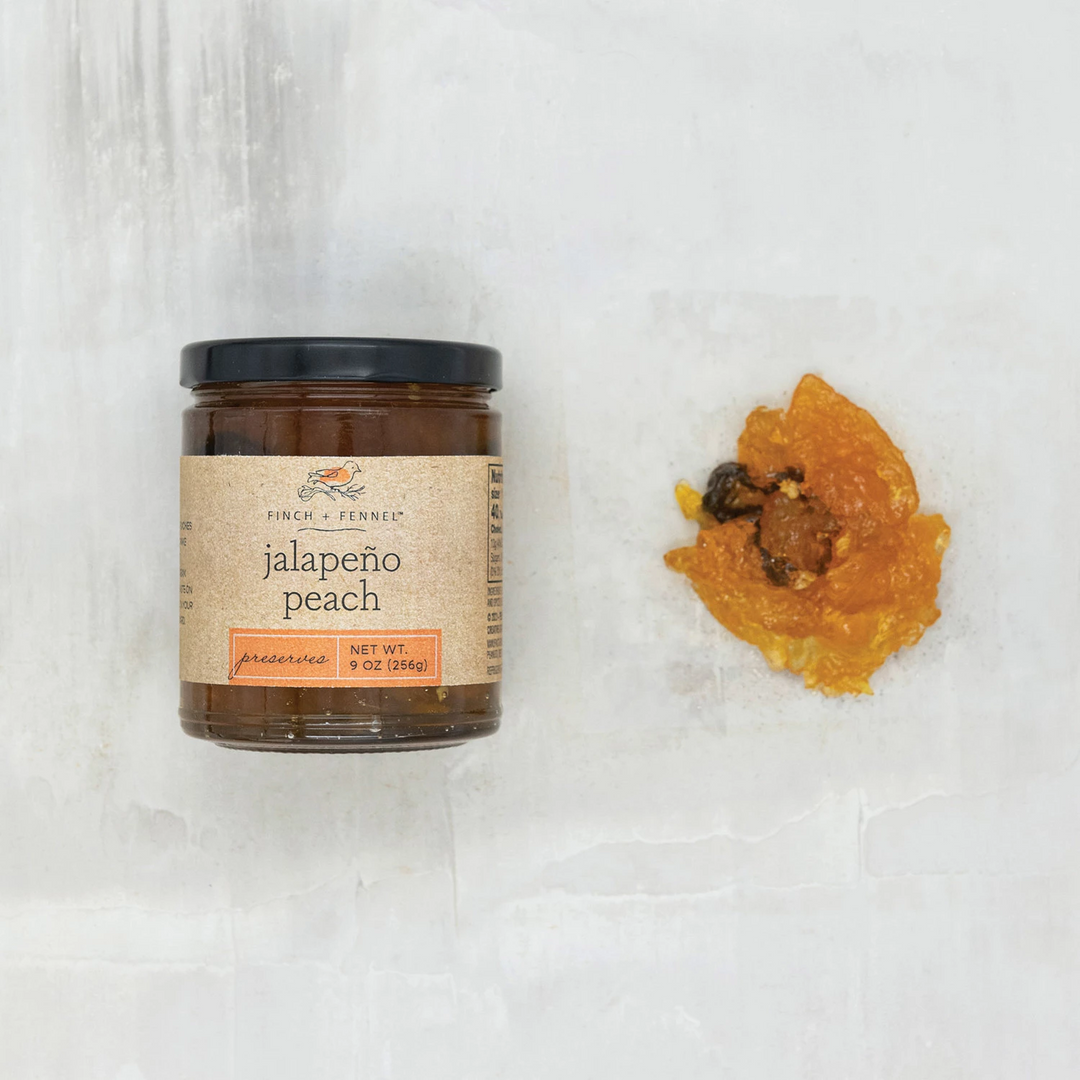 A 9 oz jar of Finch + Fennel Jalapeño Peach Preserves next to a sample of the orange jelly.