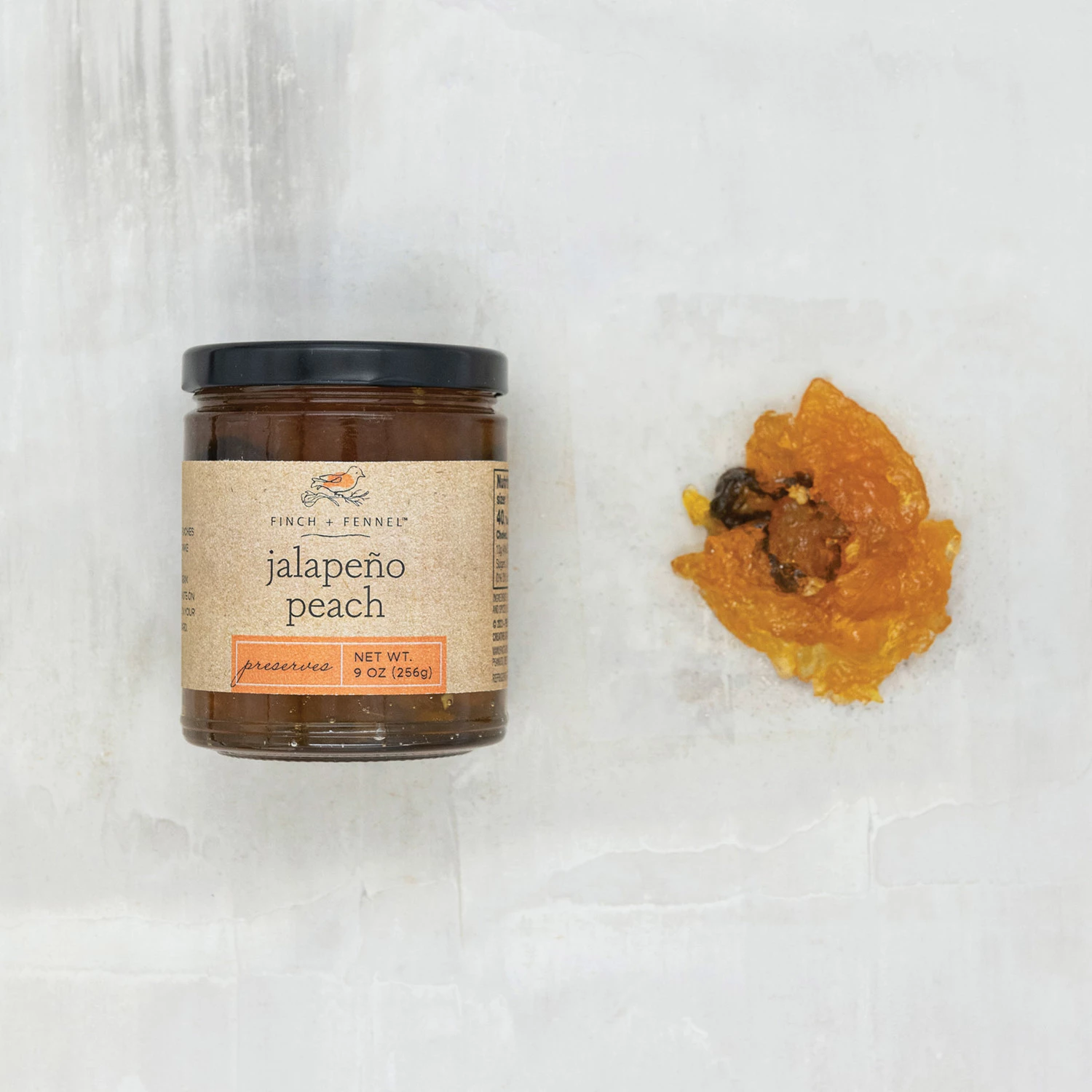 A 9 oz jar of Finch + Fennel Jalapeño Peach Preserves next to a sample of the orange jelly.