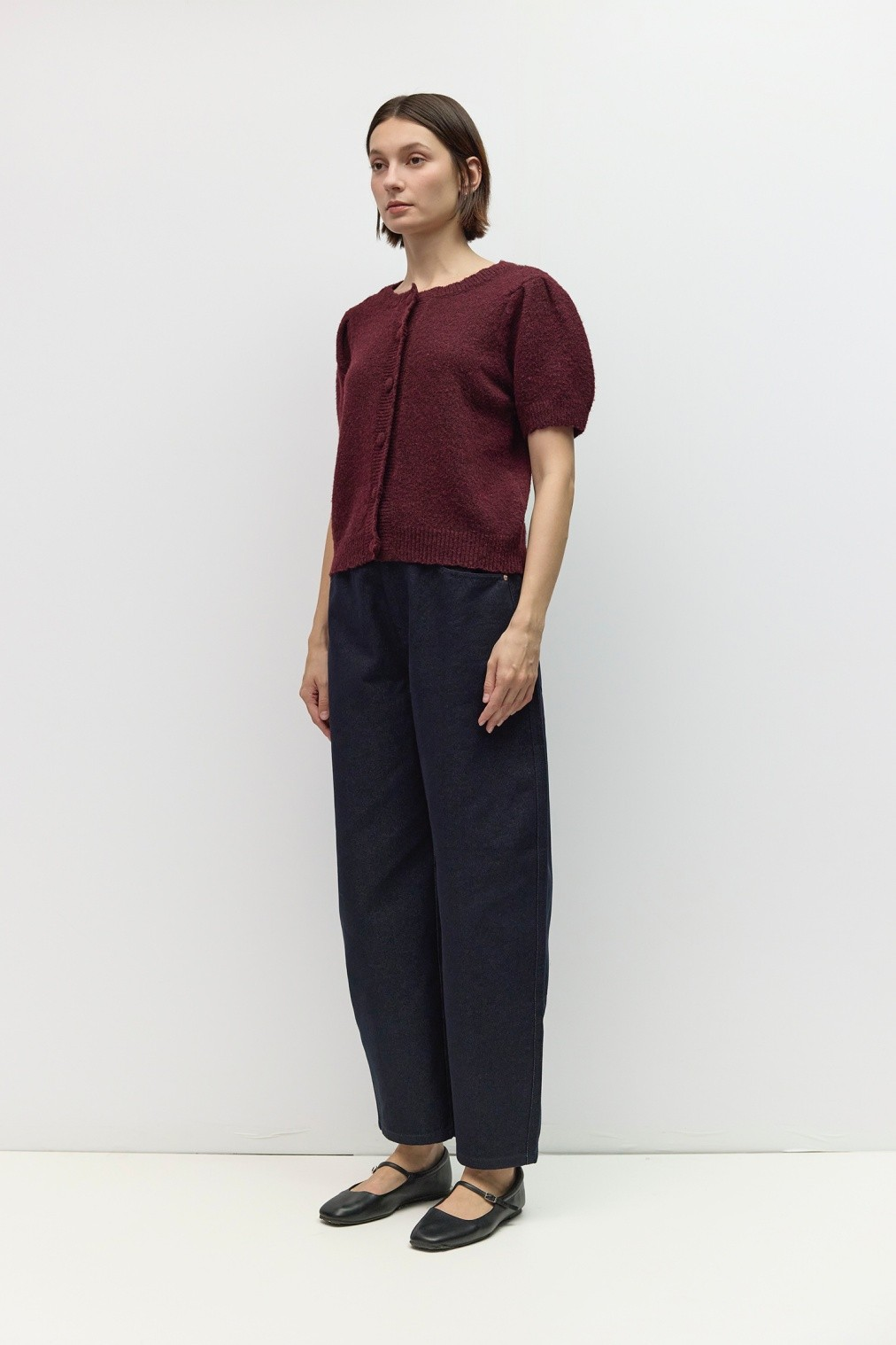 A woman wearing a burgundy short-sleeved knit button-front top with dark navy wide-leg trousers.