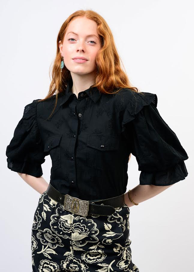 Woman wearing the black Annie Top with ruffled puff sleeves and floral patterned trousers.