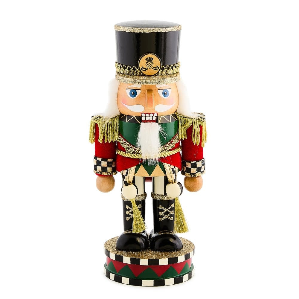Short Highland nutcracker figurine with wood body, fabric uniform in red plaid pattern, and black hat silhouette.