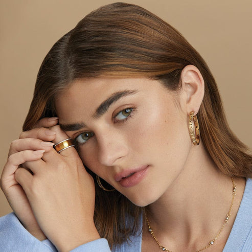 A woman wearing gold-plated Contempo Medium Hoop Earrings with artful scrollwork.