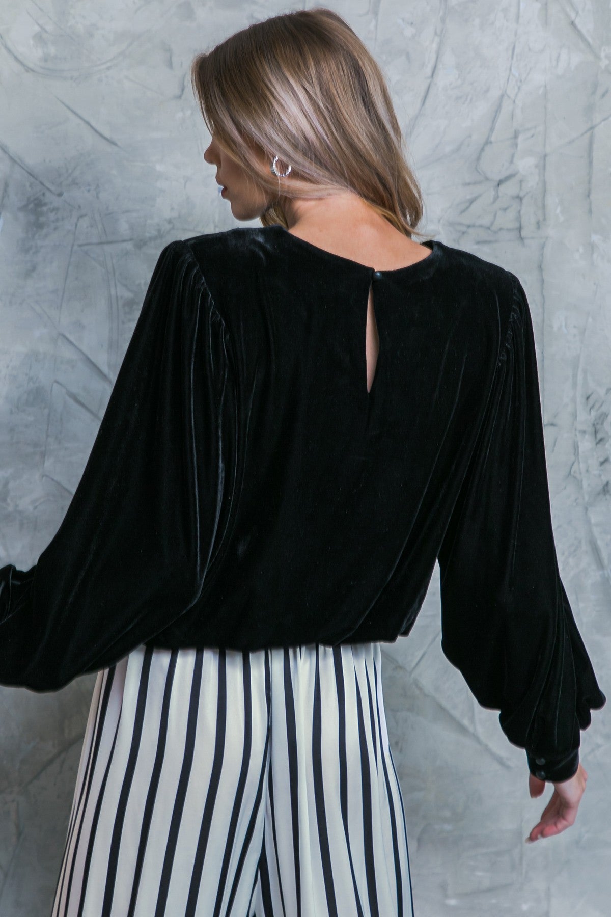 Black velvet Jenny top with long balloon sleeves and a keyhole back, paired with black and white striped pants.