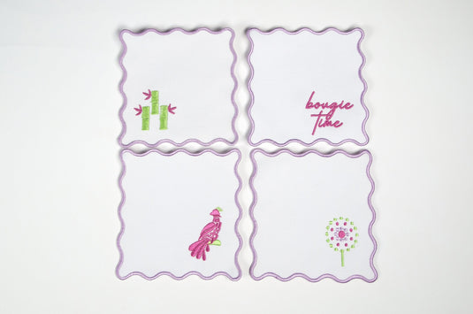 Set of four white scalloped cocktail napkins with pink and green embroidered mahjong-themed designs.