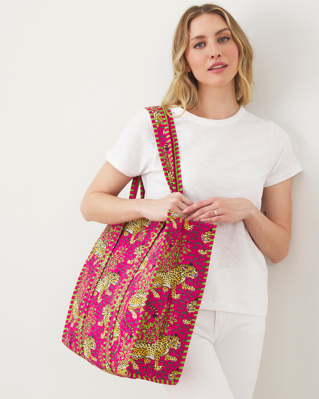 A woman wearing a white t-shirt carries a large pink leopard print Traveler Tote in Bagheera.