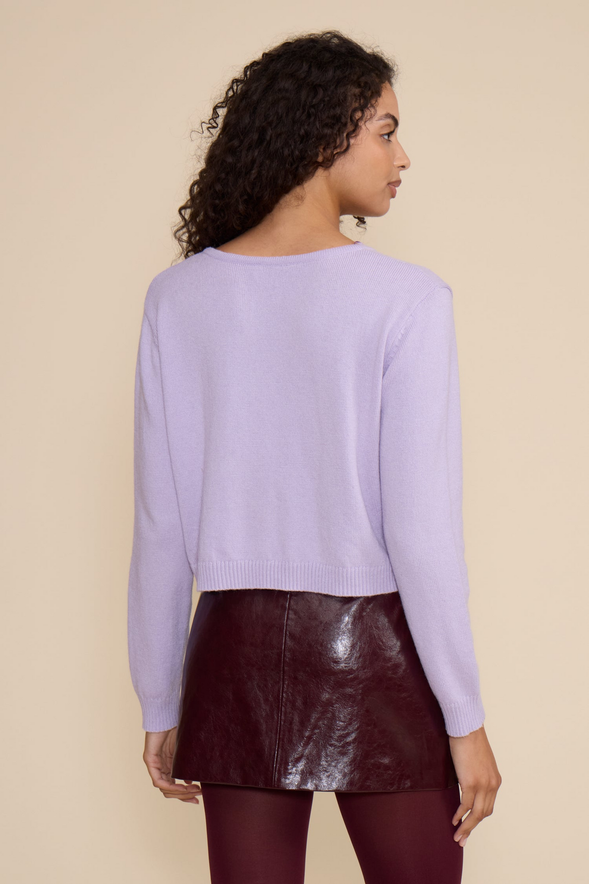 Back view of a woman wearing the light purple Lucy Judd Cardigan with a dark burgundy leather skirt.