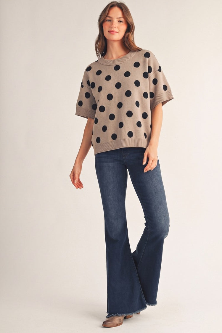 Woman wearing the Emily Polka Dot Comry Sweater Top in taupe with black dots and flared jeans.