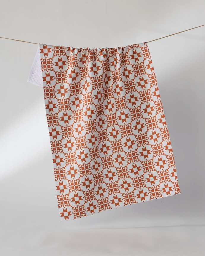 Waffle weave tea towel with an orange and white geometric star pattern hanging on a clothesline.