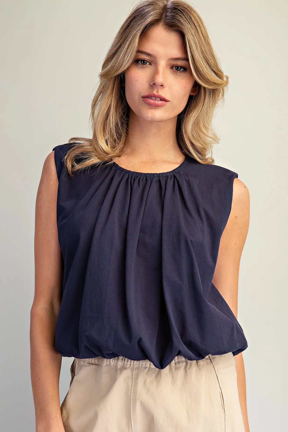 Woman wearing a navy blue Maxine Gathered Neck Bubble Hem Top with beige pants.