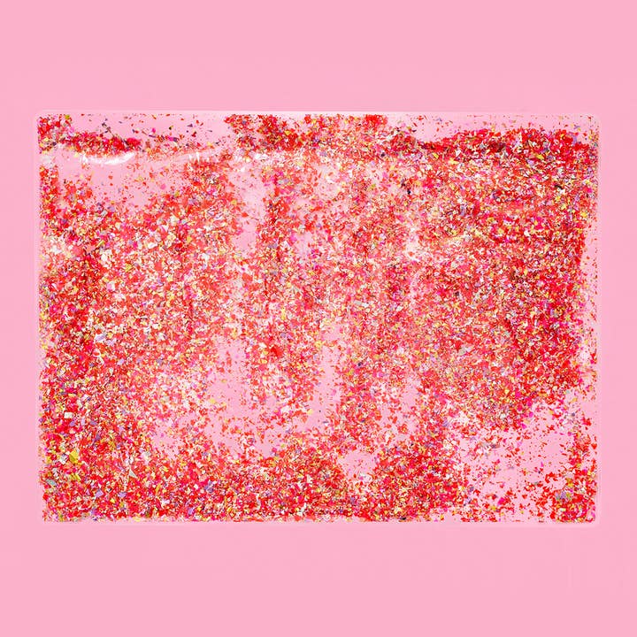 Red and pink confetti inside a clear plastic placemat measuring 18 by 13 inches.