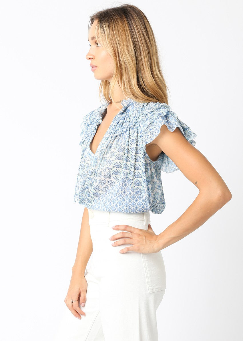 Side view of a woman wearing the Louise Top, a blue and white patterned v-neck with ruffle sleeves.