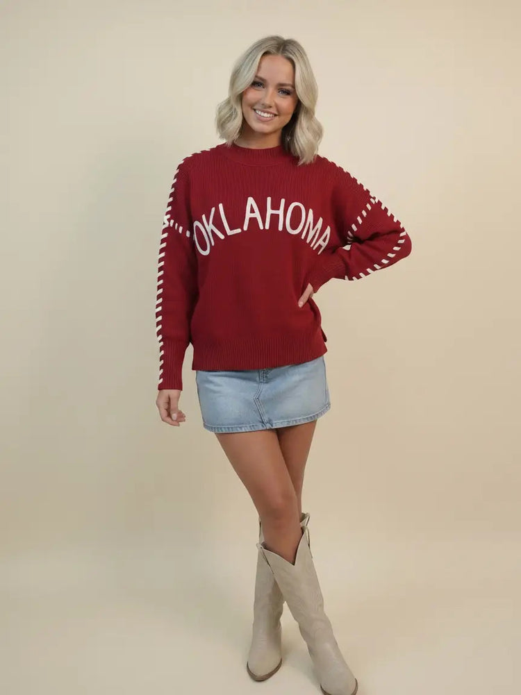 Woman in a red Paisley 'Oklahoma' whip stitch sweater with white lettering and denim skirt.