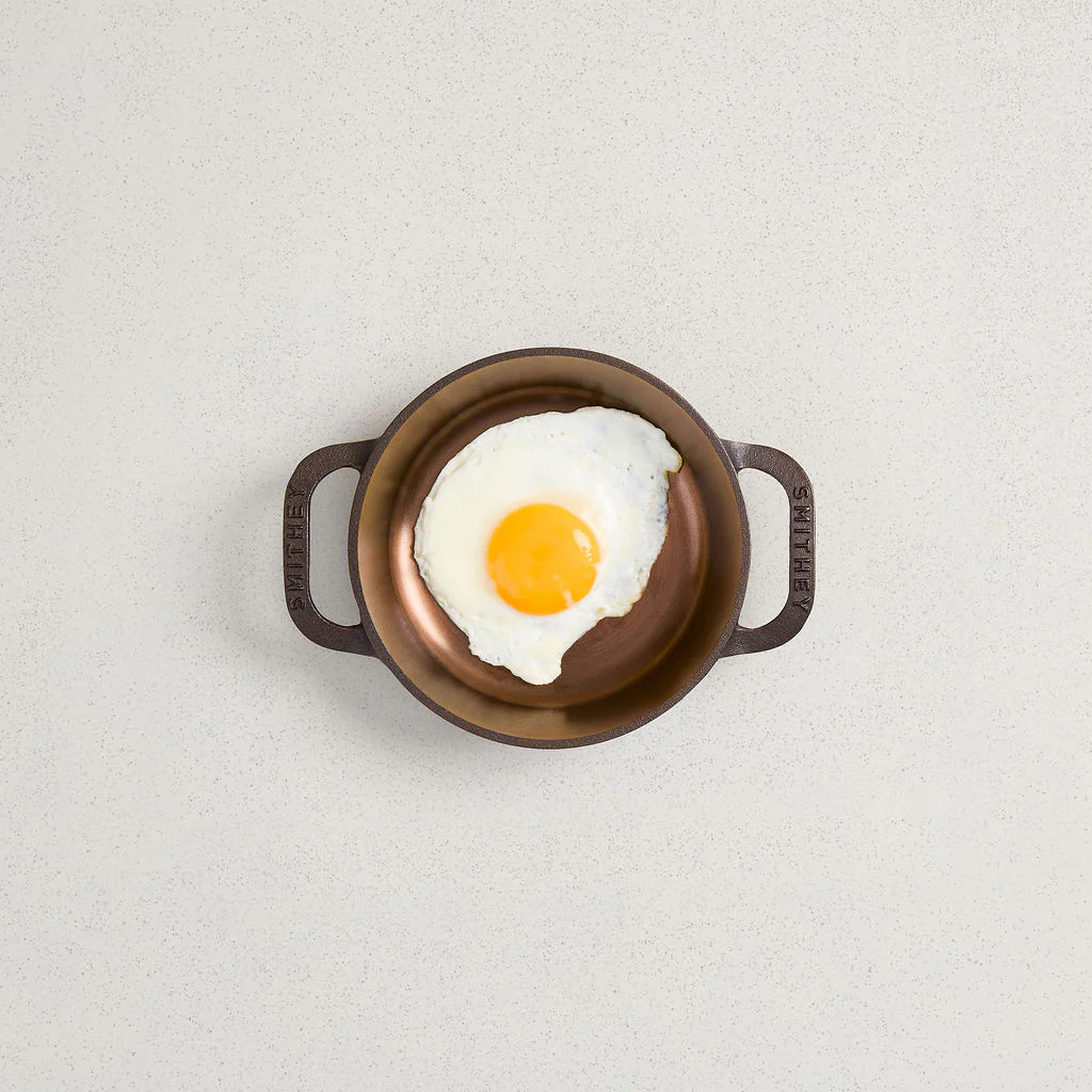 A fried egg inside a No. 6 Dual Handle Skillet with a polished finish on a light speckled surface.