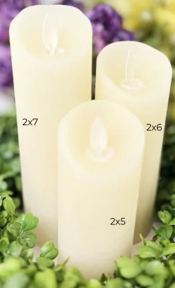Three ivory flameless LED pillar candles in sizes 2x7, 2x6, and 2x5 inches on a bed of greenery.
