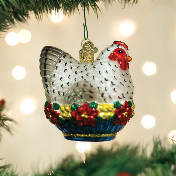 Glass French hen Christmas ornament with white feathers, red comb, and floral base on a tree.